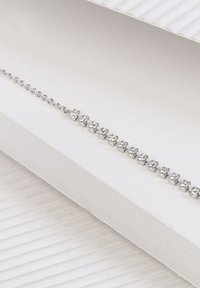 Bracelet en argent ornée de plusieurs pierres précieuses transparentes, reliées par une fine chaîne. Présenté sur un fond blanc texturé.