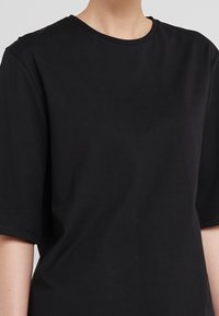 Černé bavlněné tričko s kulatým výstřihem a krátkými rukávy, které se vyznačuje hladkým povrchem a uvolněným střihem. Bez viditelných vzorů nebo akcentů.