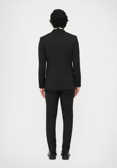 Čierny oblek so strihnutým sakom s hladkým povrchom, nohavicami s plochým prednom, a lesklými čiernymi topánkami, zobrazený zozadu.