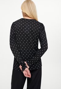 Czarna bluzka z długim rękawem w białe kropki, z okrągłym dekoltem i marszczonymi detalami na ramionach, wyeksponowana z tyłu.