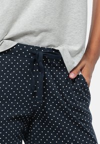 Grijs T-shirt met korte mouwen boven een marineblauwe joggingbroek met witte stippen, voorzien van een trekkoord in de taille en zijzakken. De stof heeft een gladde textuur.