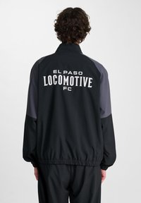 Svart och grå jacka med hög krage, elastiska ärmslut och midja; med "EL PASO LOCOMOTIVE FC" i vitt på baksidan.