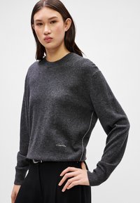 Grauer Langarm-Sweatshirt aus strukturiertem Stoff, mit rundem Ausschnitt und einem weißen Akzentstreifen an der Seite, sowie einem kleinen Logo auf der Vorderseite.