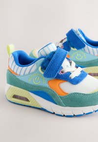 Baskets colorées pour enfants avec des bandes velcro bleues, des lacets blancs et un logo visage souriant sur le côté.