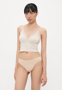 Lichtbeige hemdje met kantafwerking, aansluitend ontwerp en spaghettibandjes; gecombineerd met bijpassende lichtbeige hipsteronderbroek, gladde textuur.