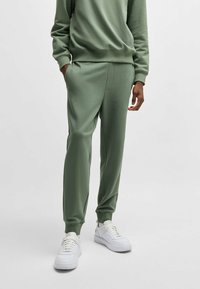 Groene joggingbroek met een elastische tailleband en boorden, voorzien van zijzakken, gecombineerd met witte sneakers. Soepele stofstructuur.