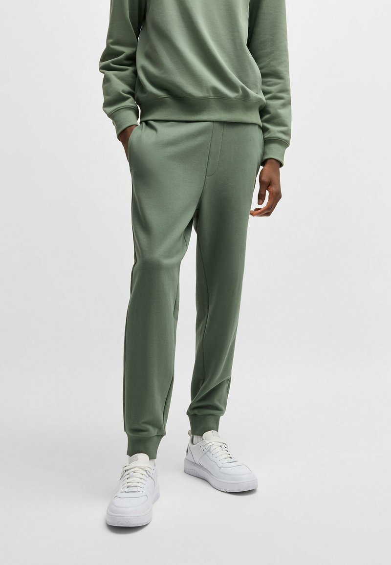 Gröna sweatpants med elastisk midja och muddar, med sidfickor, i kombination med vita sneakers. Slät tygtextur.