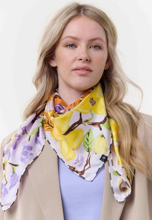 Junge Frau mit langen blonden Haaren, die eine beige Jacke und einen bunten Blumen-Schal in Gelb-, Lila- und Grüntönen um den Hals trägt.