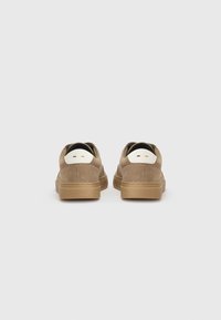 Brown suede sneakers with a smooth texture, featuring a white accent on the heel and a rubber sole. The design is low-top and casual.
