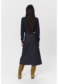 Denimkjol med lång design, mörk tvätt, slits bak och kontrasterande sömmar. Tillsammans med knähöga stövlar i senapsgul mocka.
