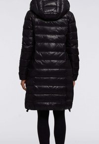 Persona che indossa un lungo cappotto imbottito nero con cappuccio, visto da dietro, abbinato a leggings neri.