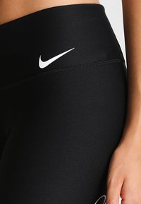 Leggings neri con logo bianco Nike swoosh, realizzati in un tessuto elastico e liscio, con vita alta e design aderente.