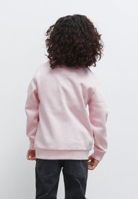 Felpa rosa chiaro con colletto rotondo e maniche lunghe, realizzata in tessuto morbido. Abbinata a pantaloni grigio scuro, vista da dietro.