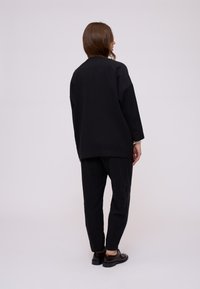Černý oversized top a odpovídající tapered kalhoty vyrobené z hladkého materiálu, s jednoduchým designem a minimálními detaily.