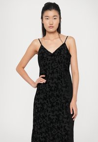 Abito nero senza maniche con un motivo floreale testurizzato. Caratterizzato da un scollo a V e una silhouette fluida. Tessuto liscio con una sovrapposizione trasparente.