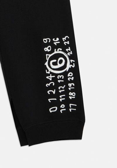 Czarne spodnie dresowe z białymi haftowanymi numerami i okrągłym symbolem na lewej nogawce. Miękka tkanina z dopasowanym ściągaczem w kostce.