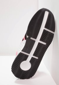 Black and white sneaker sole with pink accents; features textured rubber for grip, vertical grooves, and branding detail.