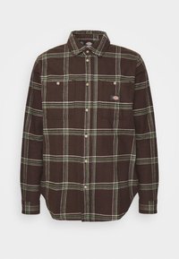 Chemise en flanelle à carreaux bruns avec des lignes vertes et blanches. Elle présente deux poches poitrine et des boutons sur le devant et aux poignets.