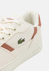 Sneaker in tela beige con accenti marroni, design con lacci, logo di coccodrillo ricamato verde e lati texturizzati, dotato di suola in gomma.