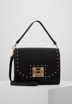 Czarna torebka z strukturalnej skóry z złotymi ćwiekami i kwadratowym zamkiem, wyposażona w górny uchwyt oraz odpinany pasek na ramię, prezentowana na białej powierzchni.