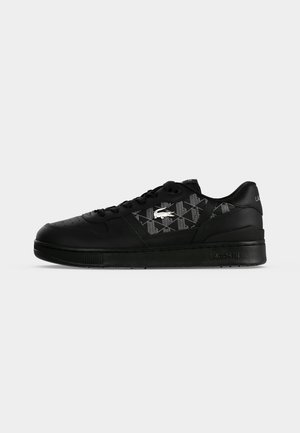 Baskets basses noires avec un panneau latéral texturé présentant un logo crocodile blanc et une semelle noire affichant le nom de la marque Lacoste.