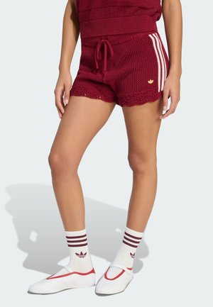 Mujer con pantalones cortos de punto granate con rayas blancas y cordón, calcetines blancos con rayas granate y zapatos blancos sin cordones.