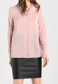Rosa Bluse mit langen Ärmeln, Knopfleiste und V-Ausschnitt, kombiniert mit einem schwarzen, figurnahen, strukturierten Rock.