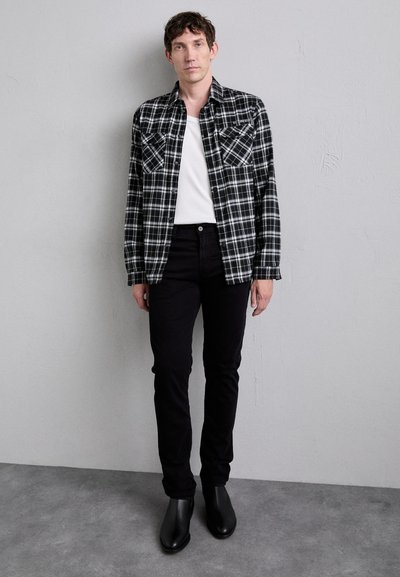 Μαύρο-άσπρο πουκάμισο καρό με δύο τσέπες στο στήθος, φορεμένο πάνω από μια λευκή μπλούζα με λαιμόκοψη crew; σε συνδυασμό με μαύρα στενά τζιν και μαύρες μπότες.