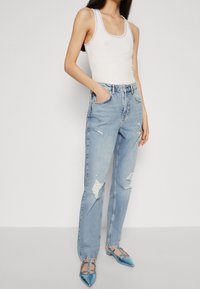 Modré roztrhané džíny s vysokým pasem, kombinované s bílým tílkem. Modré boty s špičatou špičkou a popruhy dokončují vzhled.