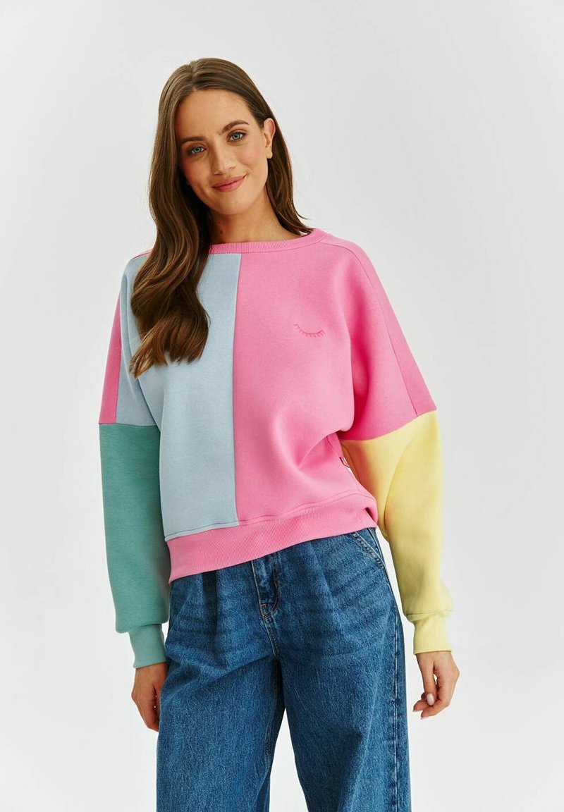 Bluza w kolorze blokowym w odcieniach różu, niebieskiego i żółtego, o luźnym kroju, okrągłym dekolcie i prążkowanych mankietach. Miękki, teksturowany materiał.