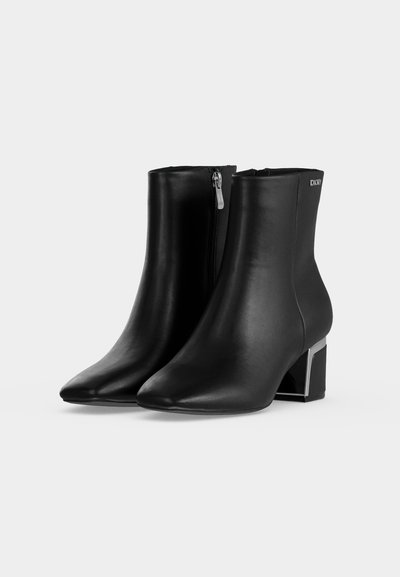 Bottines en cuir noir avec fermetures éclair latérales, bouts pointus, talons blocs avec accents métalliques et logo DKNY sur la partie supérieure extérieure.
