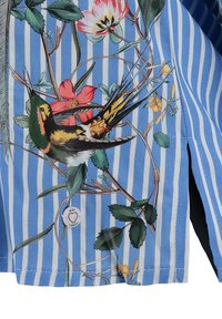 Tissu rayé bleu et blanc avec impression détaillée d'un oiseau coloré perché sur une vigne fleurie avec des feuilles vertes et des fleurs rouges et jaunes.