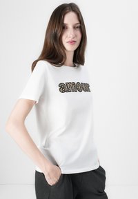 White cotton t-shirt featuring the word "amour" in a bold, leopard print design. Short sleeves and a round neck.