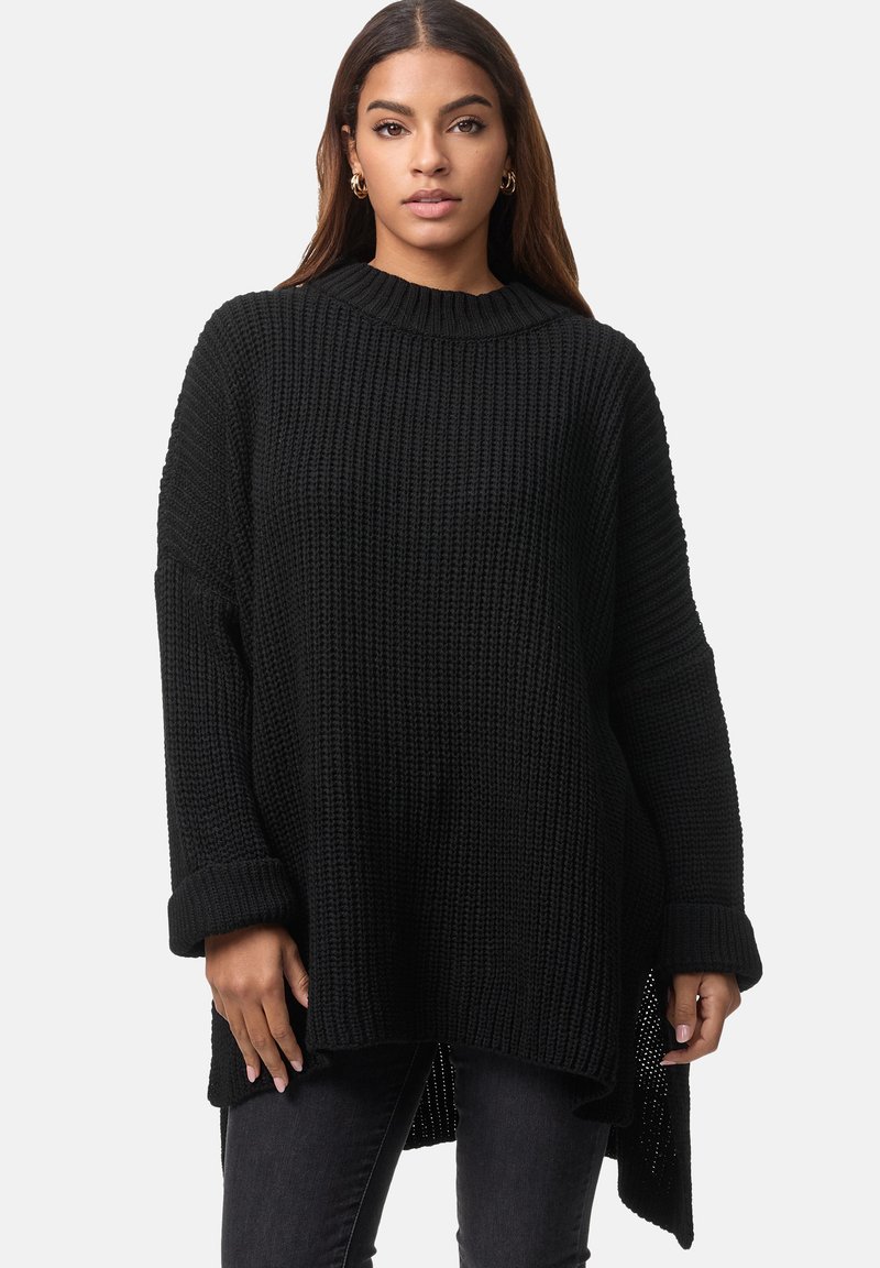 Maglione nero oversize con texture a coste, scollatura rotonda e maniche lunghe. Presenta spacchi laterali e polsini ripiegati. Abbinato a jeans scuri.
