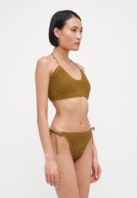 Bronzekleurige gehaakte bikini met een gemeleerd, diamantpatroon. Halter-stijl bovenstuk met golvende randen; geknoopte zijkanten van het onderstuk.