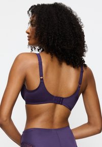 Purppuranvärinen rintaliivi säädettävillä olkaimilla, sileä tekstuuri ja hakaskiinnitys. Siinä on yksinkertainen, saumaton muotoilu ja hienovaraiset ompeludetaljit.