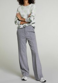 Světlounce šedý svetr se zelenými a šedými vzory srdcí a nápisem "LOVE" na manžetách, kombinovaný se širokými šedými kalhotami a bílými teniskami.