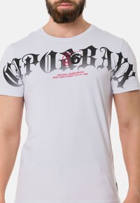 Weißes Baumwoll-T-Shirt mit großen schwarzen Grafikan text und roten Akzenten mit "Original Denim Brand", kurzen Ärmeln und Rundhalsausschnitt.