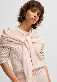 Maglione lavorato a maglia di un leggero rosa con una trama morbida e maniche corte, abbinato a una sciarpa rosa pallido drappeggiata sulle spalle.