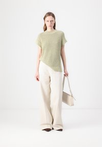 Top de punto verde claro con textura acanalada, dobladillo asimétrico, combinado con pantalones anchos crema y un bolso beige.