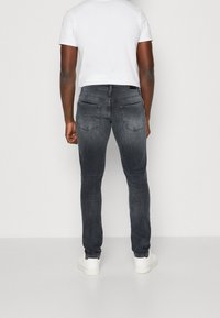 Úzké tmavě šedé džíny z denimu s kapsami na zadní straně a přiléhavým střihem. Nošeny s bílým krátkým rukávem a bílými teniskami.