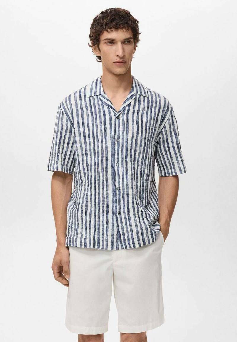 Korte mouwen shirt van lichte stof, met verticale blauwe en witte strepen, een notch kraag en een borstzak. Gecombineerd met witte shorts.