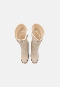 Botas altas de color beige con un exterior liso y un interior de punto acanalado. Cuentan con una puntera redondeada y un sutil detalle recogido en el eje.