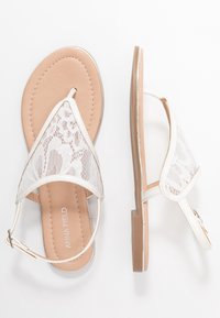 Valkeat pitsisaappaat, joissa on ohut, säädettävä nilkkahihna, sileä beige pohjallinen ja litteä kumipohja. Sisältää herkän pitsikuvion.