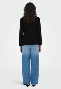 Must musta-shirt, millel on kitsenev vöökoht, koos helesiniste kõrge vöökohaga laiarööpeliste teksadega, millel on tagataskud ja kulunud viimistlus.