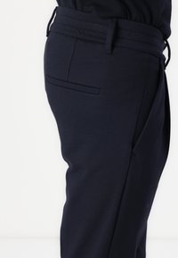 Navy blue tailored pants with a flat front, side pockets, and a smooth texture, featuring a belt looped waistband and a slim fit design.