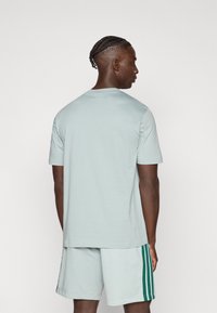 Gaiši pelēks īsroku t-krekls ar apaļu apkakli, kombinēts ar atbilstošiem šortiem ar tumši zaļām sānu svītrām. Gluda tekstūra, brīvs piegriezums.