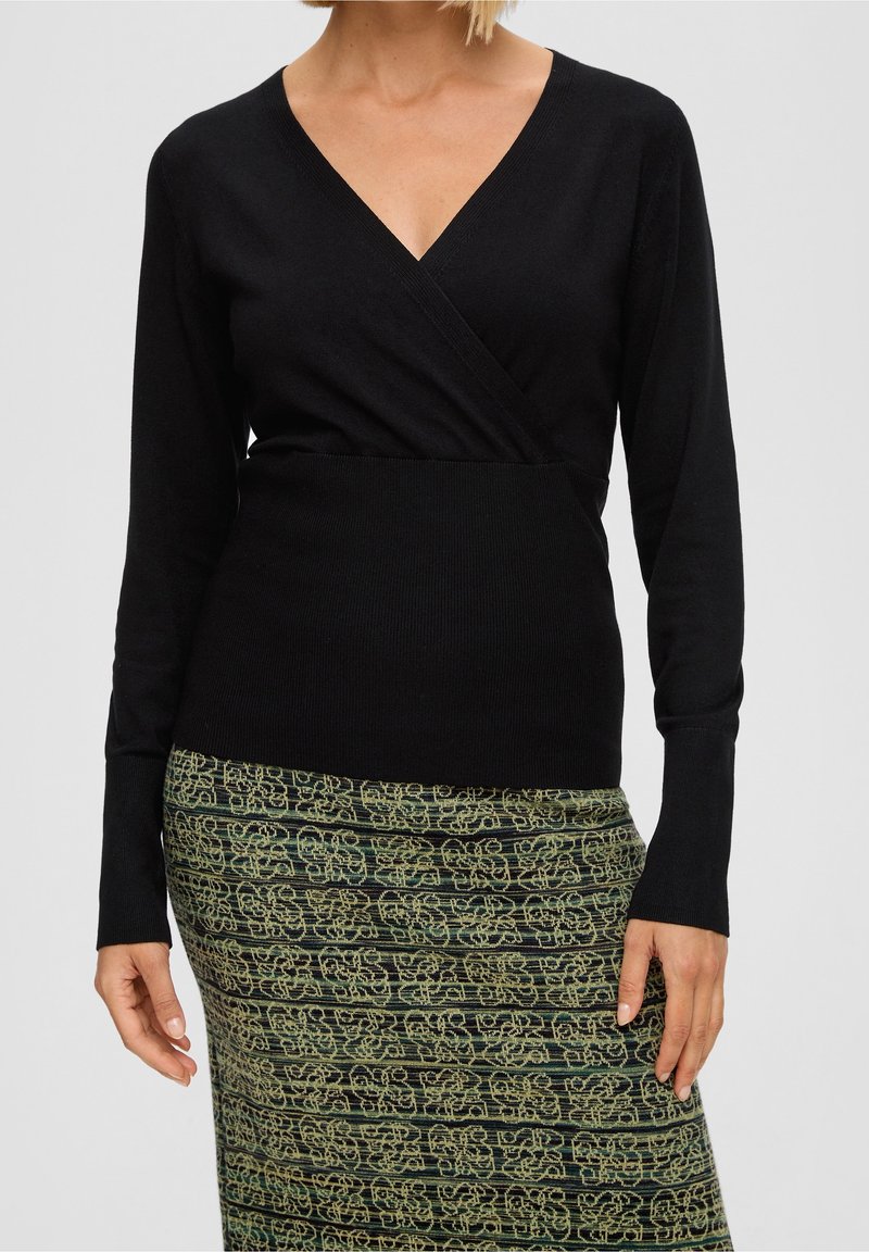 Czarna bluzka z długim rękawem i dekoltem w serek, o kroju kopertowym. Materiał wydaje się gładki i lekko dopasowany, zestawiony z wzorzystą zieloną spódnicą.