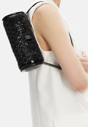 Osoba nosící bílý top bez rukávů nese na rameni černý válcový texturovaný kožený batoh.