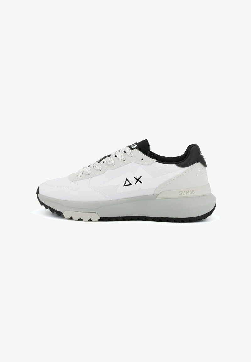 Zapatilla deportiva baja blanca y gris con lengüeta de talón negra, cordones blancos con patrón y logotipo geométrico negro en el lateral.